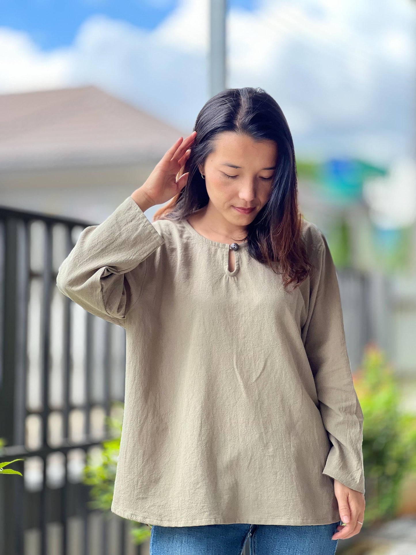 May include: A long-sleeved, light brown, loose-fitting shirt with a keyhole neckline and a button detail.