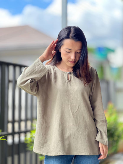 May include: A long-sleeved, light brown, loose-fitting shirt with a keyhole neckline and a button detail.