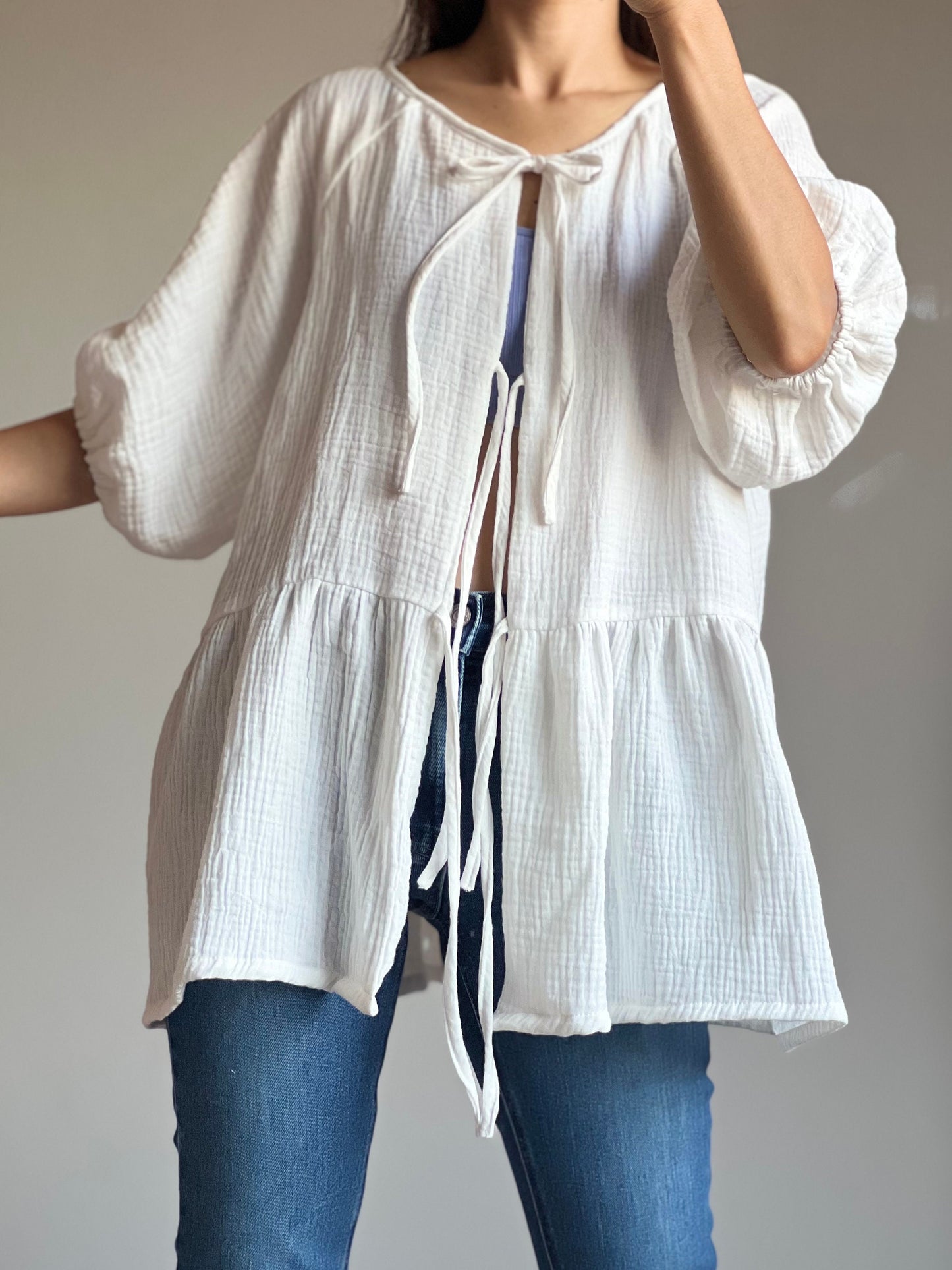 May include: A white cotton gauze peasant top with a tie at the neckline. The top has a ruffled hem and 3/4 sleeves. The top is worn over blue jeans.