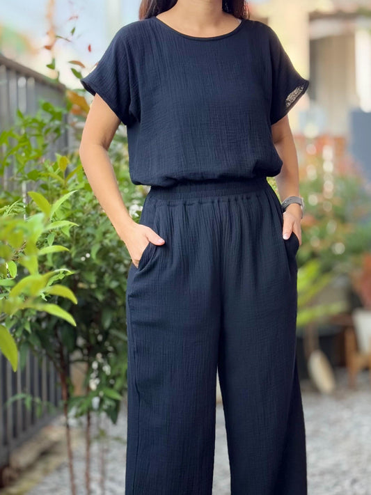May include: A black jumpsuit with a short-sleeved top and wide-leg pants. The top has a round neckline and the pants have a drawstring waist.