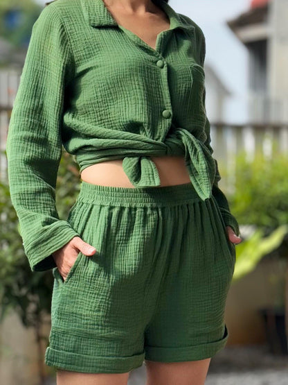 May include: Green cotton gauze pajama set.  The set includes a long-sleeved button-down shirt and shorts. The shirt is tied at the waist. The shorts have a comfortable elastic waistband and cuffed hems.  The fabric has a textured appearance.